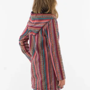 Sett bakifrån bär en person med vågigt hår Coline damjacka med fleecefoder - en lång, färgglad jacka med huva och vertikala ränder i rött, blått och orange - tillsammans med blå jeans.