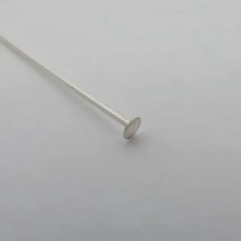 En Hattpinnar 25-50mm/0,51 huvudnål i sterlingsilver vilar på en slät, ljusgrå yta. Den har ett tunt, rakt skaft i sterlingsilver och ett platt, runt huvud - perfekt för smyckestillverkning.