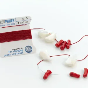 En rulle Smycketråd Griffin Nylon Power Svart med vita snäckpärlor och röda korallpärlor som delvis är uppträdda på den svarta nylontråden, plus några lösa pärlor, mot en vit bakgrund.