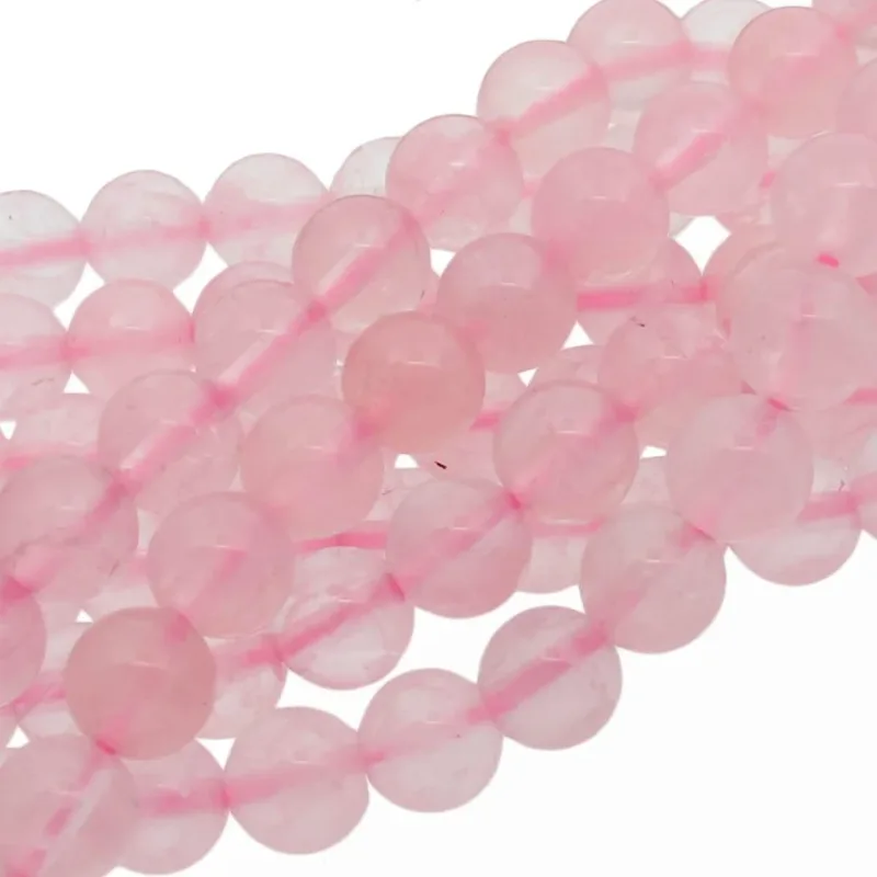 Närbild av flera trådar med runda, polerade rosa rosenkvartspärlor, arrangerade i lätt överlappande rader mot en vit bakgrund.