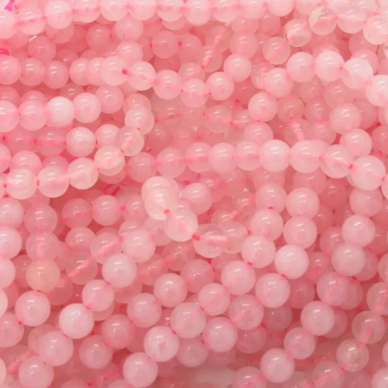 Närbild av ett stort antal runda, rosa pärlor, möjligen av rosenkvarts, tätt uppträdda med en synlig rosa tråd. Pärlorna har en slät, glansig yta och ett mjukt, genomskinligt utseende.