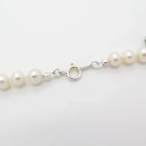 En närbild av Knutgömma sterlingsilver 3mm pärlhalsband visar ett silverfärgat fjäderringlås och flera runda, vita pärlor mot en vit bakgrund, med betoning på det detaljerade låset.