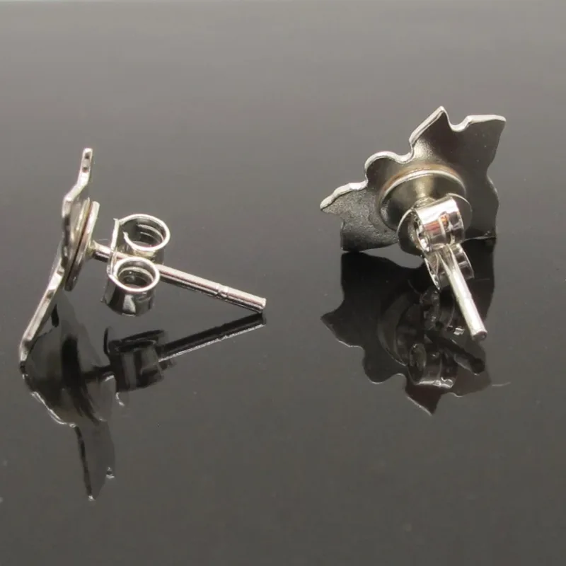 Ett par Örstift med platta 5mm i Sterlingsilver visas på en blank svart yta, med ett örhänge liggande platt och det andra upprätt, och visar både fram- och baksidan tillsammans med sina stolpar.