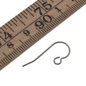 En Öronkrok i Titan 19mm - Allergisäker ligger bredvid en linjal och visar sin längd på 19 mm. Titankroken har en böjd ovansida och en liten ögla nedtill för att fästa smycken.