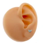 En närbild av en realistisk öronmodell med Örhänge med stift - Fjäril, en liten blå fjärilsformad stiftörhänge som visas på örsnibben.