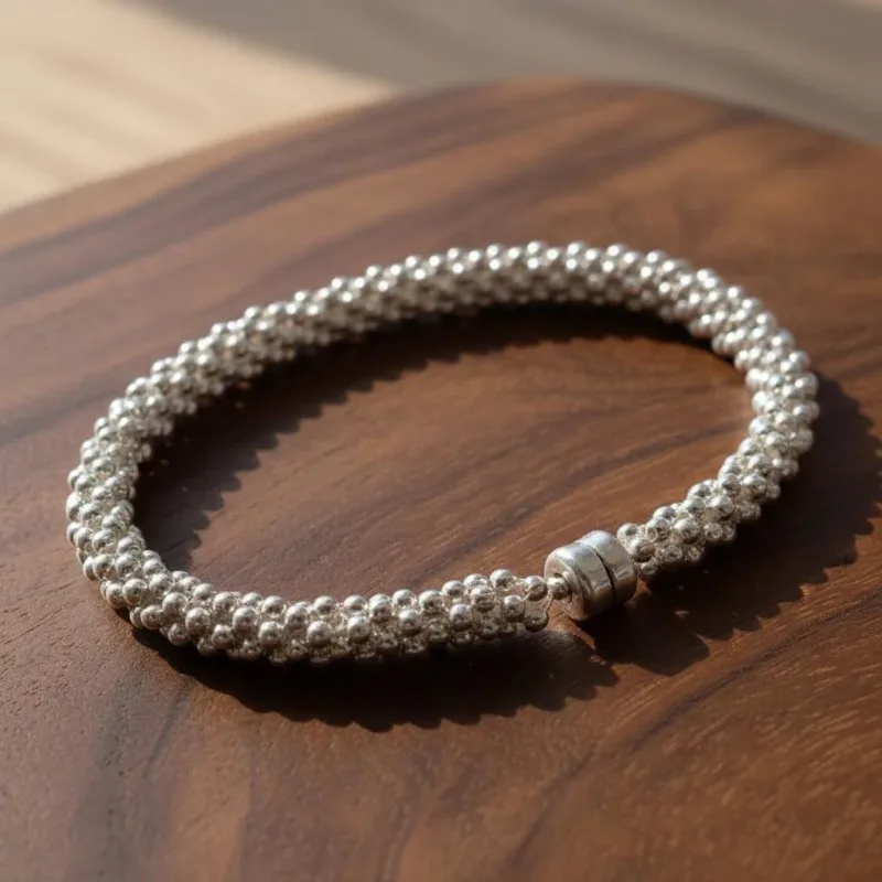 Ett Silverpärlor runda blanka 2mm/0,9mm armband med ett cylindriskt lås vilar på en träyta och skiner i naturligt solljus.