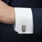 En person i mörk kostym och vit skjorta har en Manschettknapp i Rostfritt stål, en manschettknapp i rostfritt stål, på sin skjortmanschett.