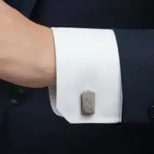 En person i mörk kostym och vit skjorta har en Manschettknapp i Rostfritt stål, en manschettknapp i rostfritt stål, på sin skjortmanschett.