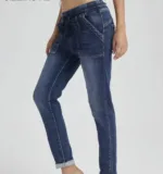 En person modellerar Jogger Jeans elastisk byxa-högmidjiga blå jeans med framfickor och dragsko i midjan-stående med ett ben lätt böjt mot en ljus bakgrund.