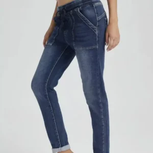 En person modellerar Jogger Jeans elastisk byxa-högmidjiga blå jeans med framfickor och dragsko i midjan-stående med ett ben lätt böjt mot en ljus bakgrund.