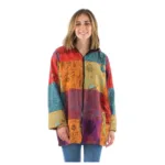 En kvinna med axellångt hår ler mot kameran i blå jeans och Färgglad patchwork bomullsjacka, en livfull bomullsjacka med färgglada rutor och mönster. Bakgrunden är enfärgad vit.