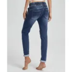 En person står barfota mot en ljus bakgrund, sedd bakifrån, iklädd Jogger Jeans elastisk byxa-blå jeans med upprullade ben, bakfickor och resår i midjan.