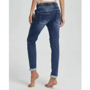 En person står barfota mot en ljus bakgrund, sedd bakifrån, iklädd Jogger Jeans elastisk byxa-blå jeans med upprullade ben, bakfickor och resår i midjan.