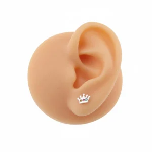 En öronmodell i silikon visar Örhänge Prinsesskrona med kristaller, ett kronformat stiftörhänge med röda, gula och blå ädelstenar på örsnibben mot en vit bakgrund.