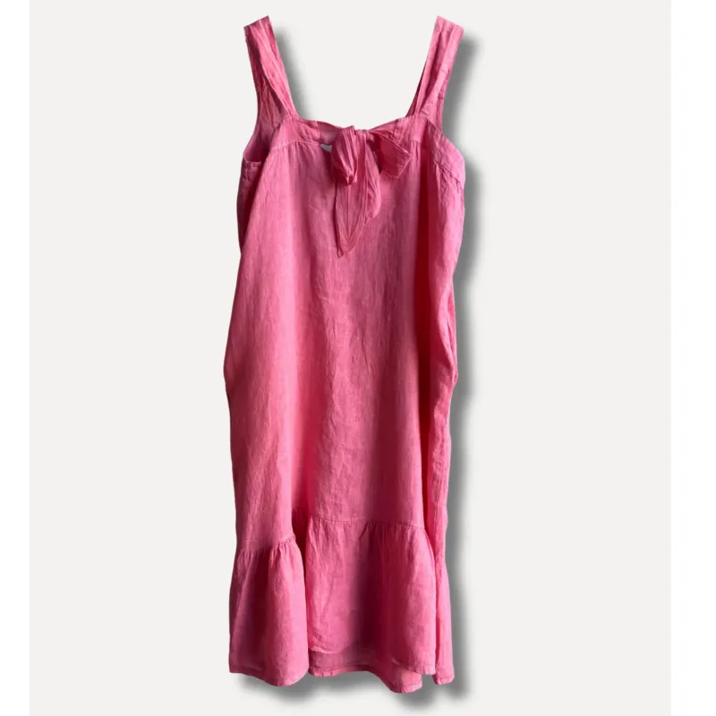 Linneklänning Sicily underbar sommarklänning är en ärmlös rosa linneklänning med breda axelband, knytband i halsringningen och volang i nederkanten, mot en vit bakgrund.