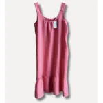 Linneklänning Sicily underbar sommarklänning: Ärmlös rosa klänning med rund halsringning, rynkad hals och volang i nederkant. Med vit tagg med svart text vid halsringningen. Visas mot en enfärgad ljus bakgrund.