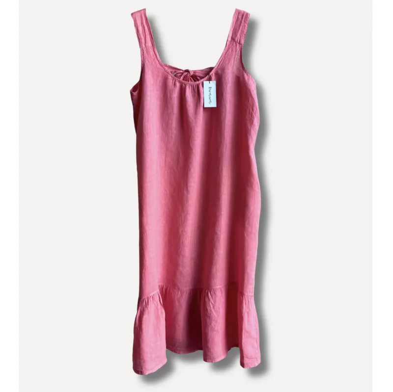 Linneklänning Sicily underbar sommarklänning: Ärmlös rosa klänning med rund halsringning, rynkad hals och volang i nederkant. Med vit tagg med svart text vid halsringningen. Visas mot en enfärgad ljus bakgrund.