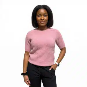 Woman wearing a pink textured short-sleeve sweater and black drawstring pants, standing with one hand in her pocket and looking at the camera.