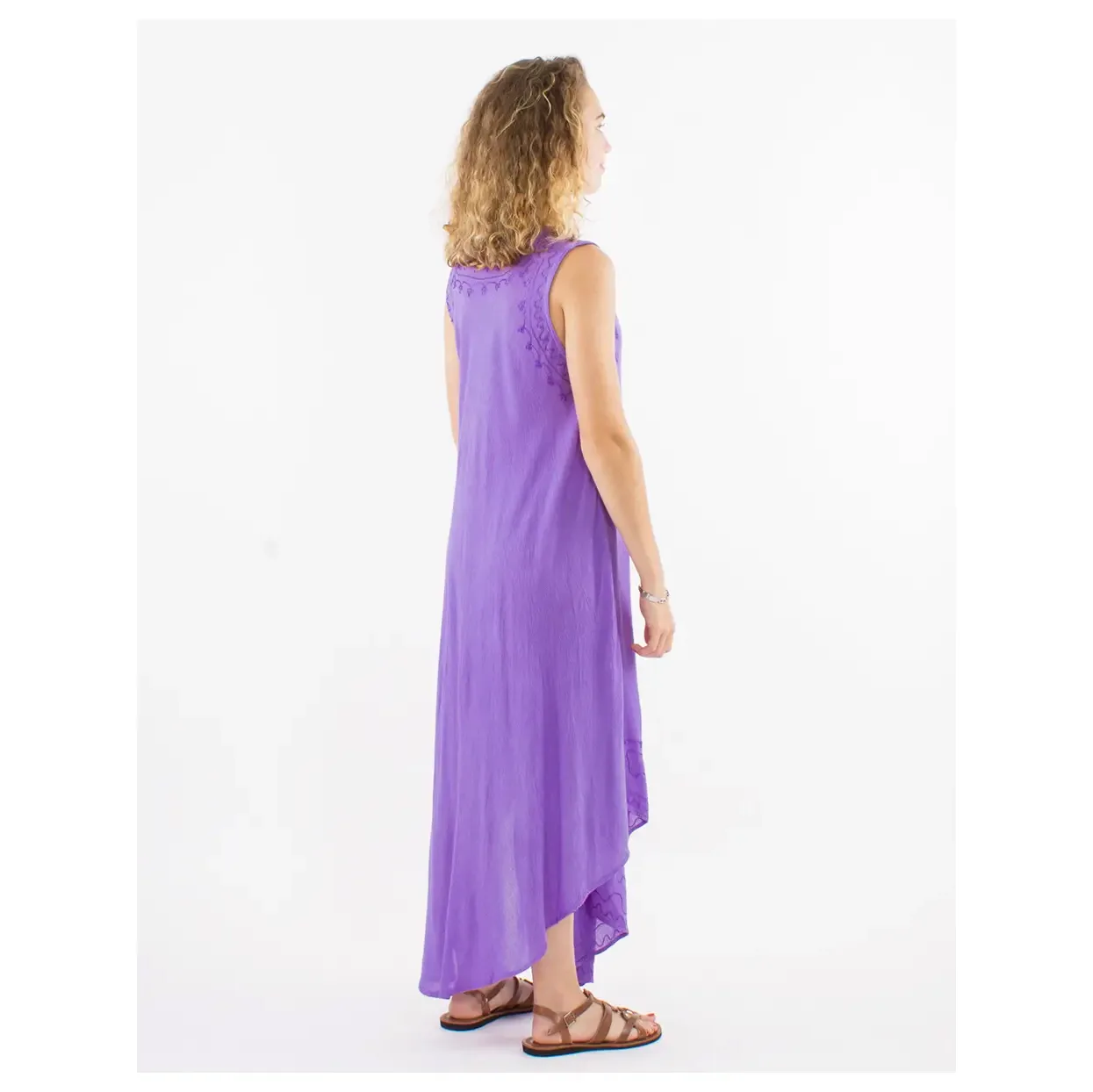 Woman standing in a purple sleeveless maxi dress with lace detail on the back, wearing brown sandals (side view).
