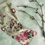 Floral fabric with pink peonies and green leaves laid over a pale green surface, with a branch in the background.