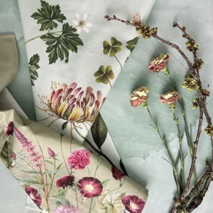 Assorted botanical-printed fabrics in soft pastel tones with pink flowers and green leaves laid on a light surface.