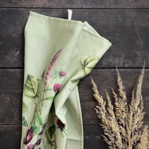 Light green floral scarf draped on a dark wooden surface with dried grasses beside it.