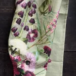 Light-green fabric with a botanical floral print, featuring purple flowers and pink blooms laid on a dark wooden surface.