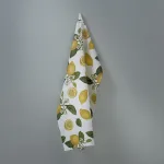 White towel with a bright lemon and green leaf pattern hanging on a gray wall.