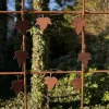 Girlang Murgröna för armeringsnät 4 Rusty iron fence with leaf-shaped metal ornaments hanging on wires, set against a green garden backdrop.