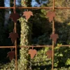 Rusty iron fence with leaf-shaped metal ornaments hanging on wires, set against a green garden backdrop.