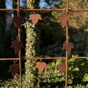 Rusty iron fence with leaf-shaped metal ornaments hanging on wires, set against a green garden backdrop.
