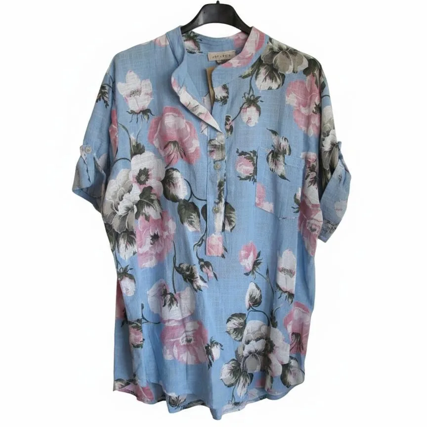 Annie Ljust Blå Blommig Bomullsskjorta 6 Blue floral button-front tunic blouse on a hanger, showing pink and white flowers on light-blue fabric