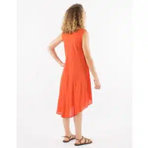 Woman in an orange sleeveless midi dress, seen from the back, standing with one hand on hip and wearing strappy sandals.