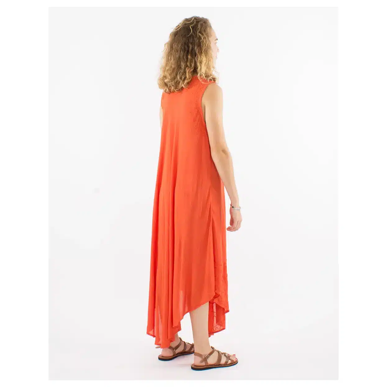 Woman in an orange sleeveless maxi dress with a high-low hem, standing sideways in brown sandals.