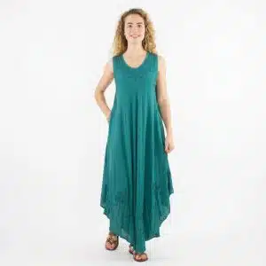 Woman wearing a teal sleeveless maxi dress with embroidery, standing against a white studio background with a relaxed pose.