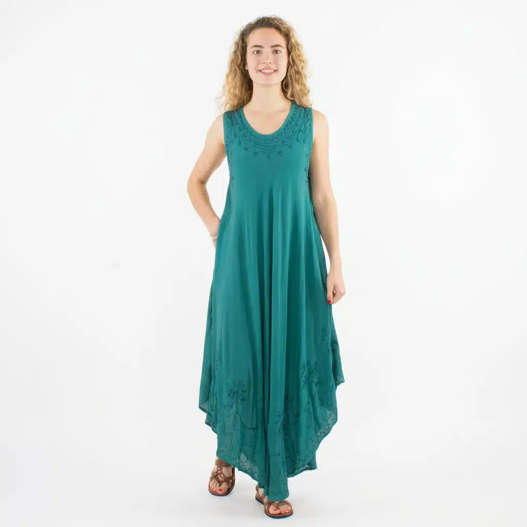 Woman wearing a teal sleeveless maxi dress with embroidery, standing against a white studio background with a relaxed pose.