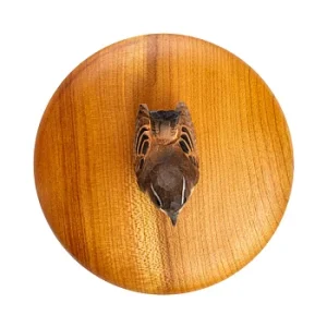 Circular wooden plaque with a central carved animal head and warm wood grain texture.