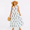 Woman wearing a sleeveless white maxi dress with blue motifs, paired with a straw hat and woven handbag