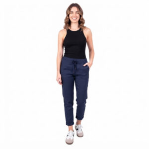 1787233391383 - Fredrix Design & Smyckerian Woman in a black sleeveless top and navy drawstring jogger pants, standing with one hand in pocket and smiling.