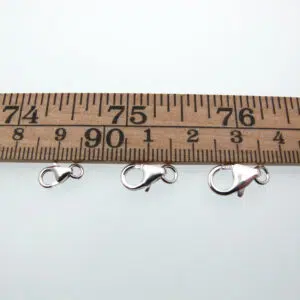 Wooden ruler showing inches with three silver lobster clasps laid below the 7–9 inch marks.