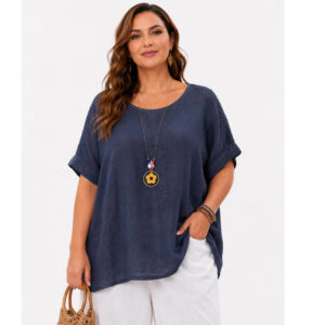 Woman wearing a navy loose linen top and white pants, accessorized with a sunflower pendant necklace and a woven straw bag