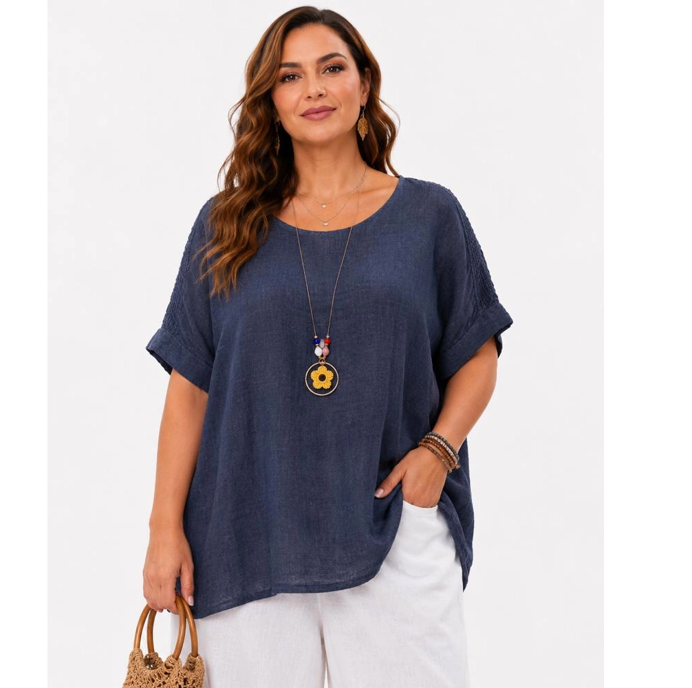 Woman wearing a navy loose linen top and white pants, accessorized with a sunflower pendant necklace and a woven straw bag