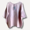 Light pink linen blouse with a blue tag hanging from the back neckline, photographed against a pale background