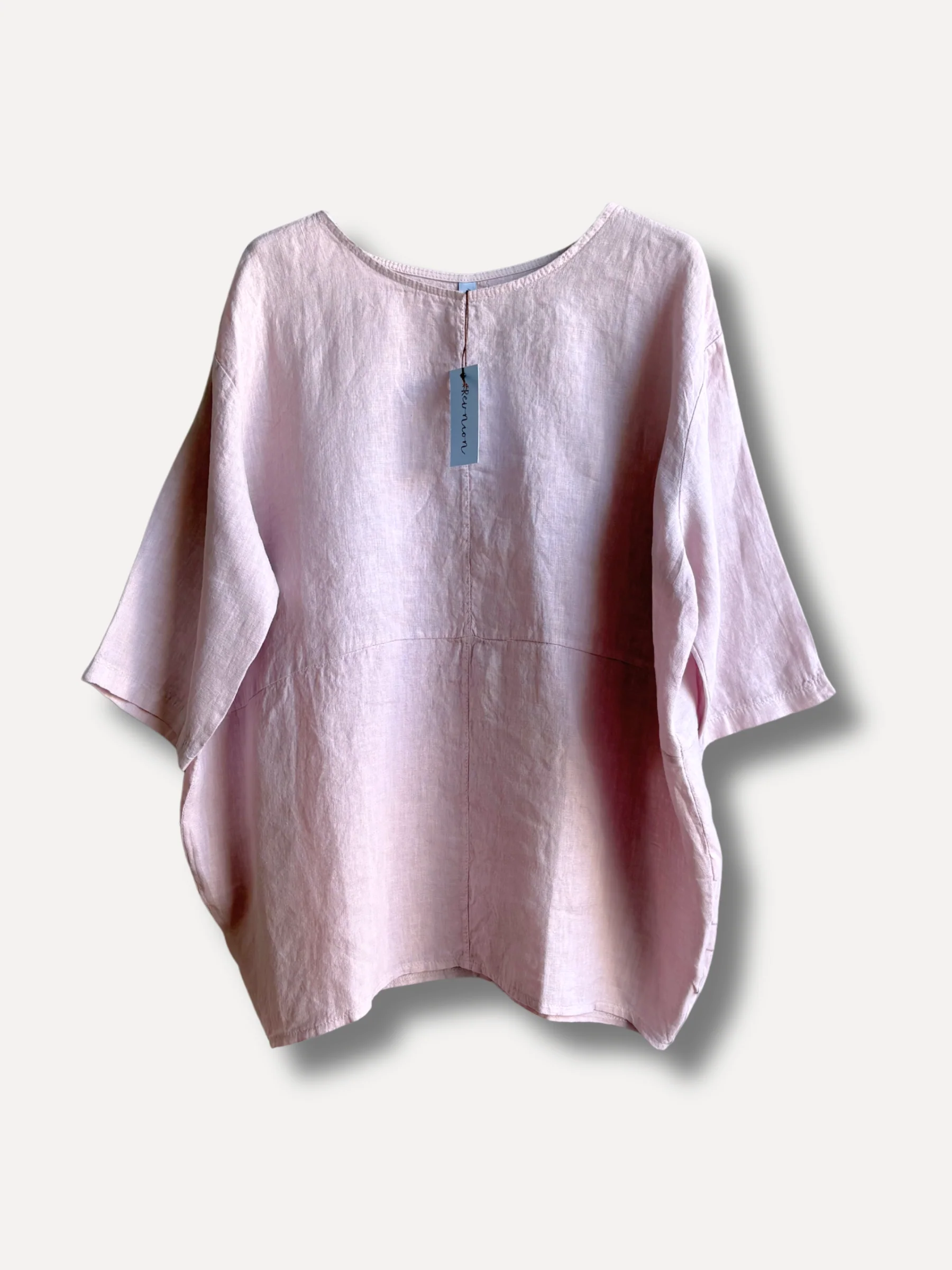 Light pink linen blouse with a blue tag hanging from the back neckline, photographed against a pale background