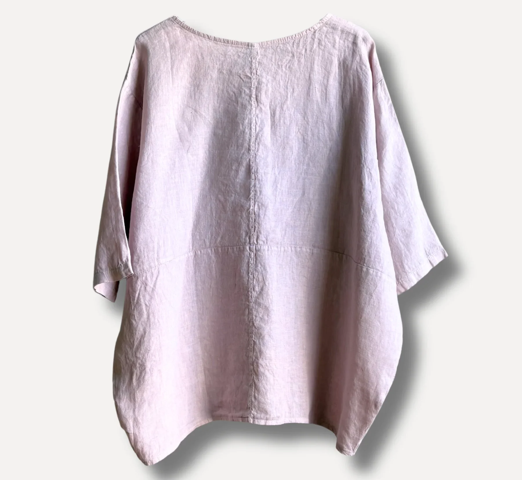 Back view of a light pink linen blouse with loose sleeves and a center seam running down the back.