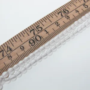 Close-up of a wooden ruler laid diagonally with a strand of clear glass beads beside it.