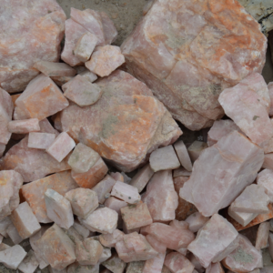 IMG_2222 - Fredrix Design & Smyckerian Pile of pink rose quartz rocks and broken stones scattered on dusty ground.